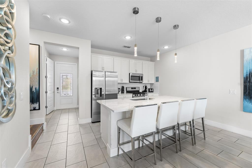 A modern kitchen features white cabinetry, stainless steel appliances, and a large island with seating — 856 DRIVING RANGE COURT, REUNION, FL