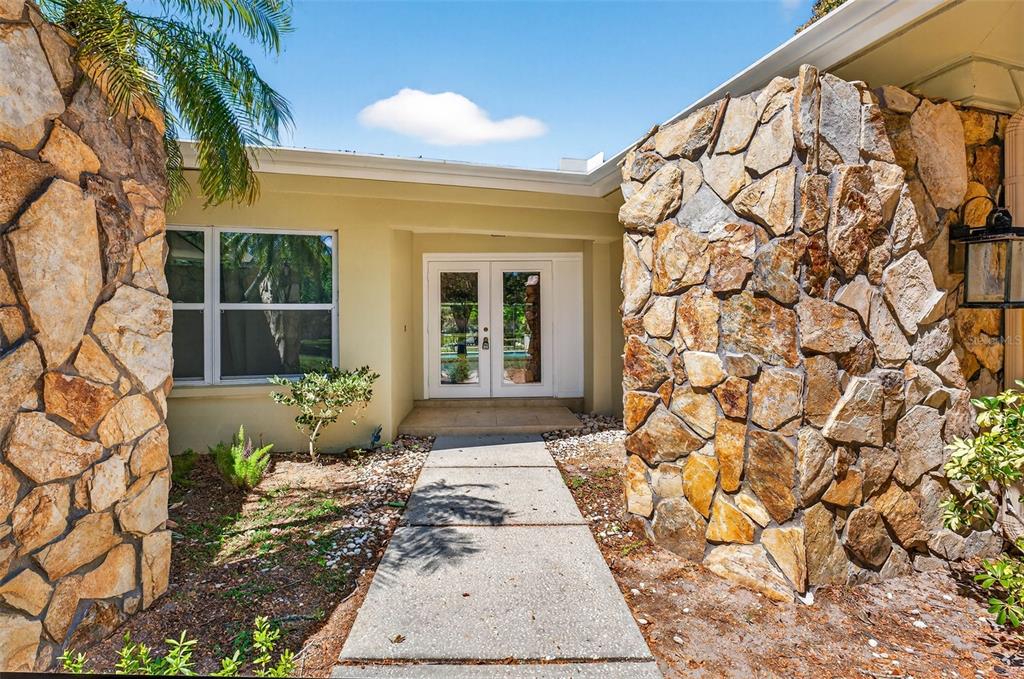 A concrete walkway leads to the double-door entrance of a house with stone-clad exterior walls — 2111 PADDOCK CIRCLE, DUNEDIN, FL