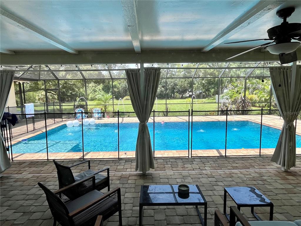 A covered patio with a pool enclosure overlooks a swimming pool and a grassy backyard — 2111 PADDOCK CIRCLE, DUNEDIN, FL