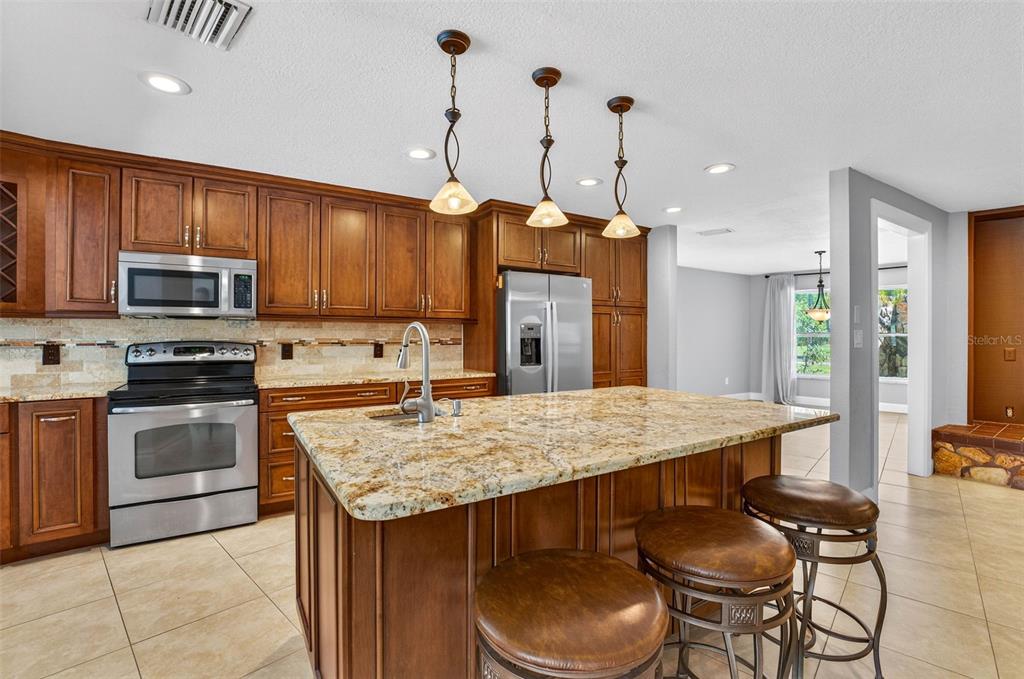 A kitchen with wood cabinets, granite countertops, a center island, and stainless steel appliances — 2111 PADDOCK CIRCLE, DUNEDIN, FL