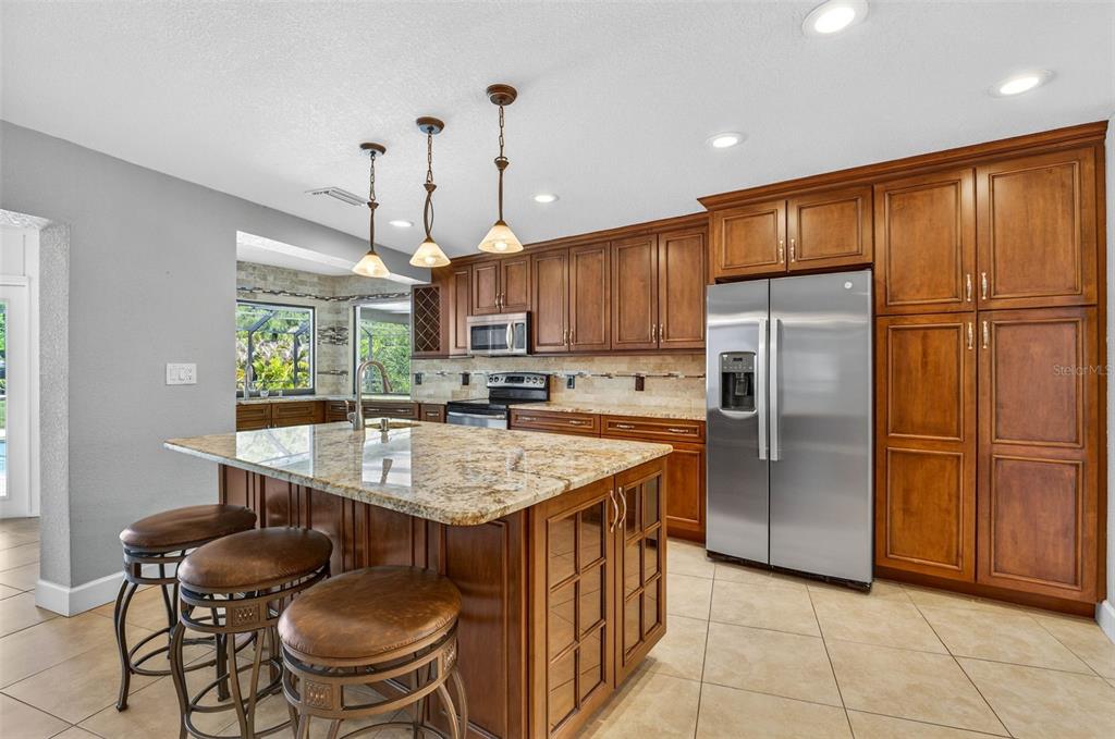 A kitchen with wood cabinets, granite countertops, a center island with stools, and stainless appliances — 2111 PADDOCK CIRCLE, DUNEDIN, FL