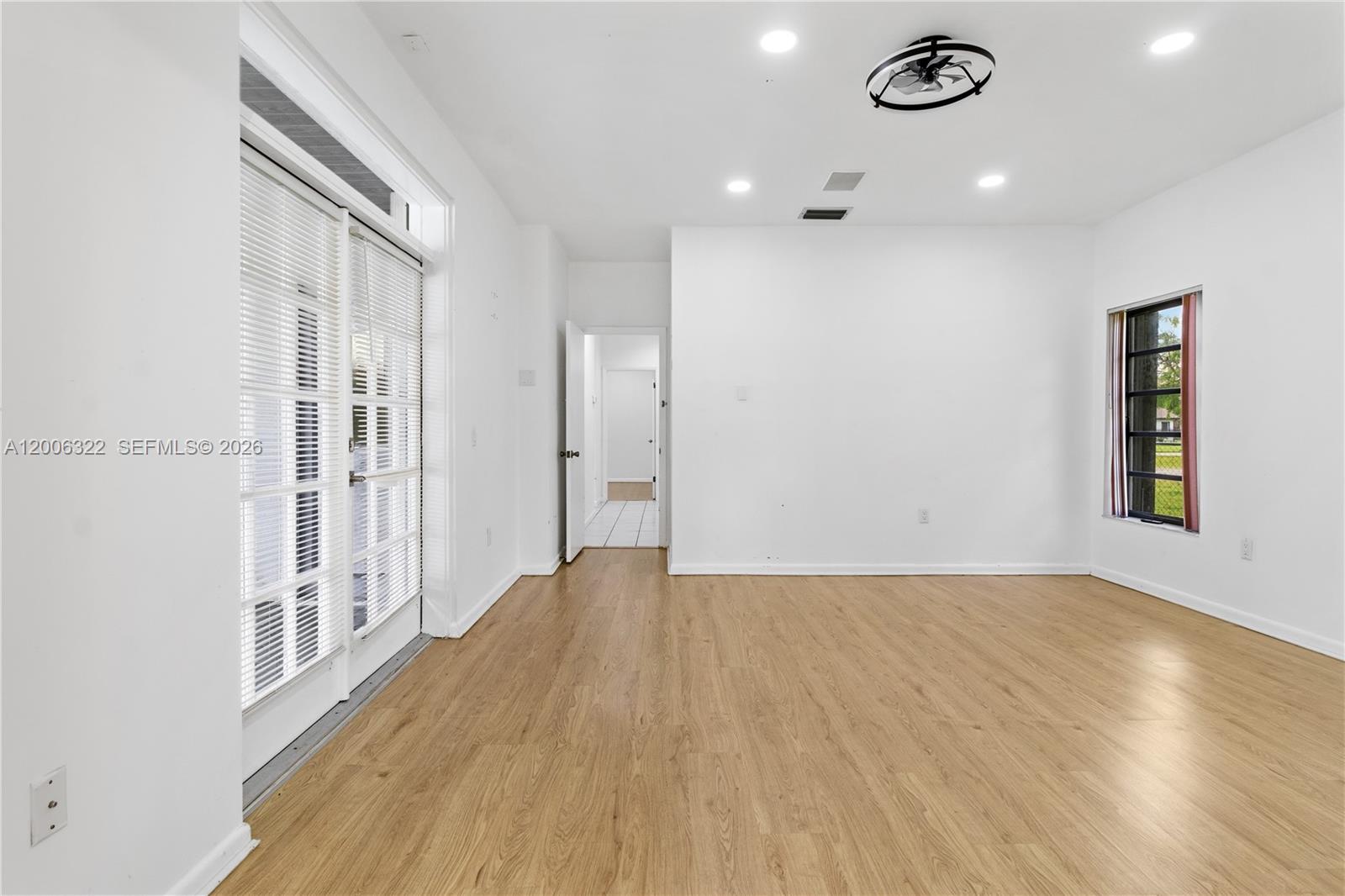 An empty room features light wood-look flooring, white walls, recessed lighting, and glass doors — 15941 SW 252nd St, Homestead FL 33031, HOMESTEAD, FL