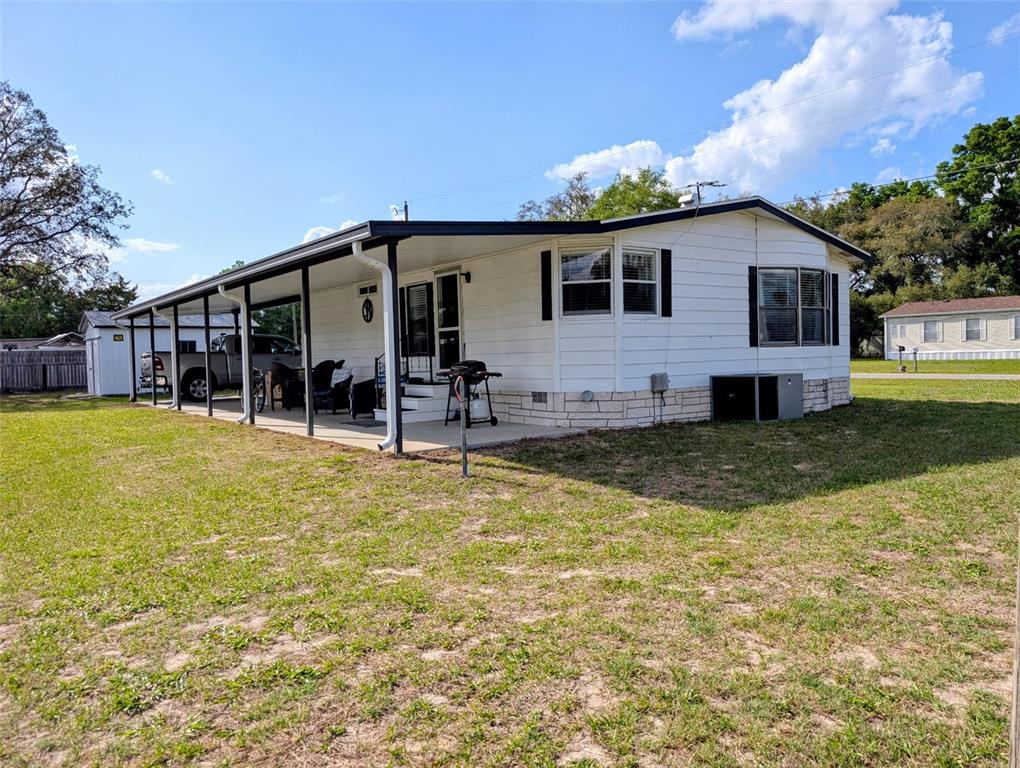 A white mobile home features a covered carport, a stone-patterned base, and a grassy yard — 9300 SE 140TH PLACE, SUMMERFIELD, FL