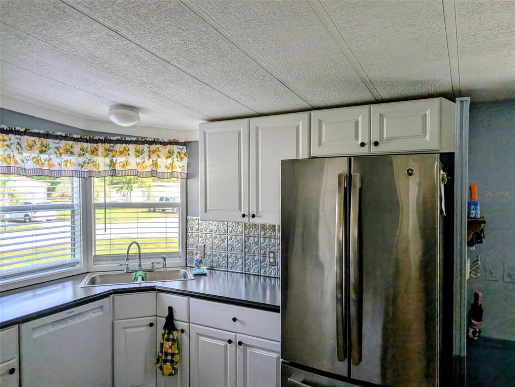 A kitchen features white cabinets, stainless steel appliances, a corner sink, and a patterned backsplash — 9300 SE 140TH PLACE, SUMMERFIELD, FL