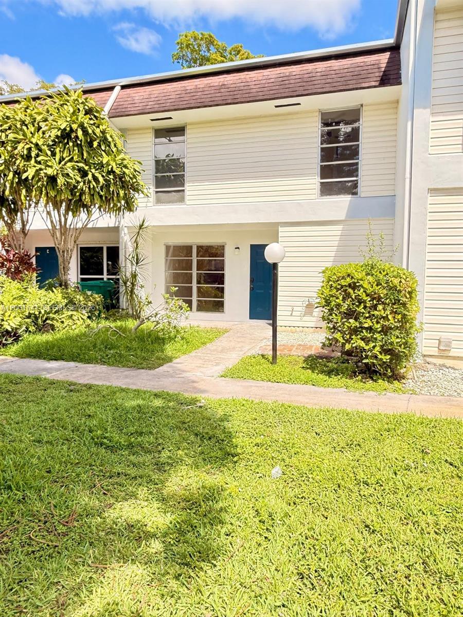 A two-story townhouse exterior with light siding, a blue front door, and a front lawn — 3301 Raleigh St # 4D, Hollywood FL 33021, HOLLYWOOD, FL