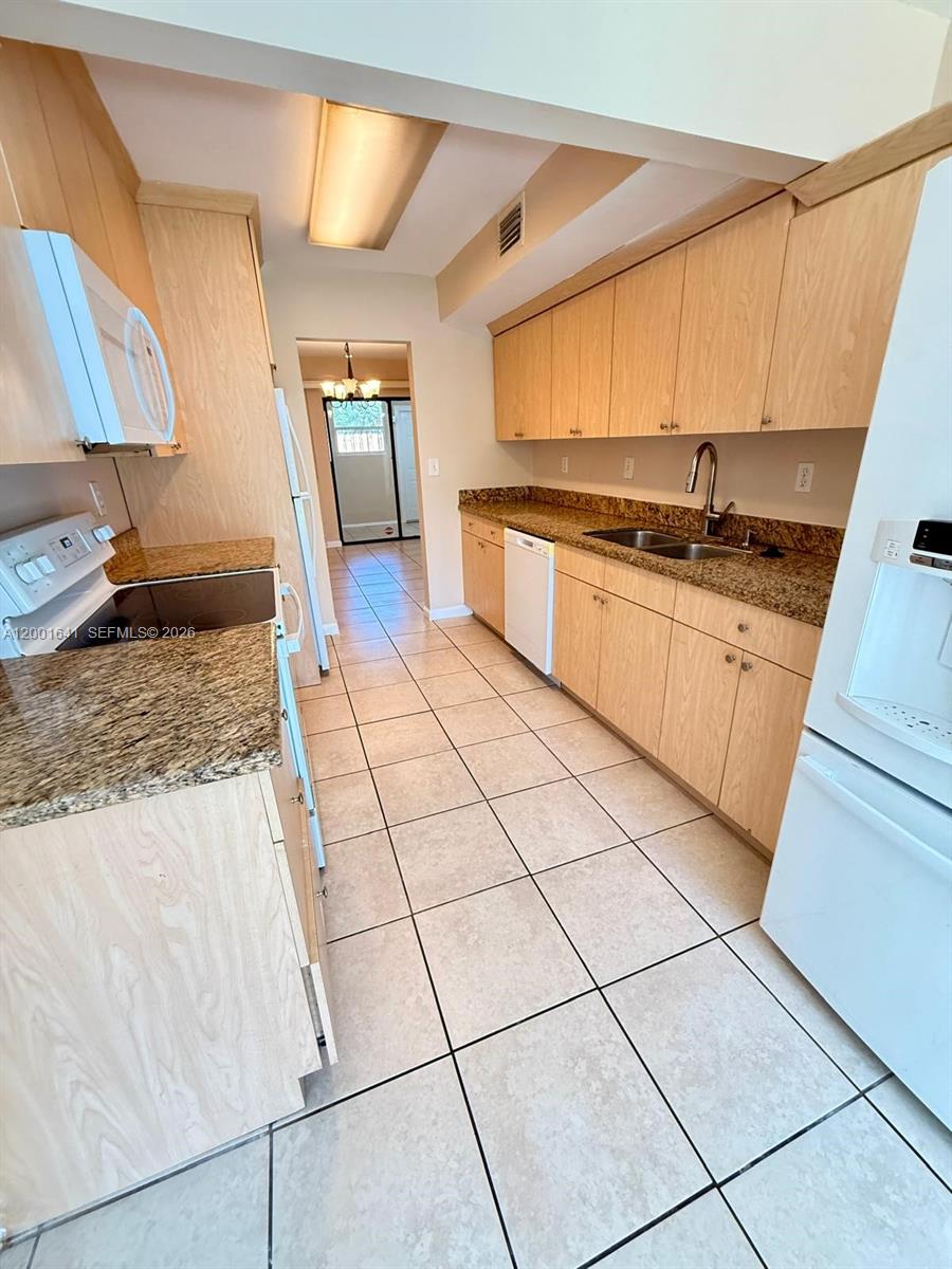 A galley-style kitchen features light wood cabinets, granite countertops, and light-colored floor tiles — 3301 Raleigh St # 4D, Hollywood FL 33021, HOLLYWOOD, FL
