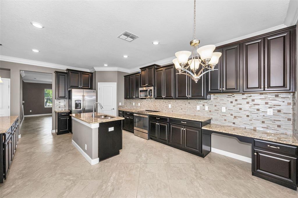 A kitchen with dark wood cabinets, granite countertops, stainless steel appliances, and a central island — 11923 CINNAMON FERN DRIVE, RIVERVIEW, FL