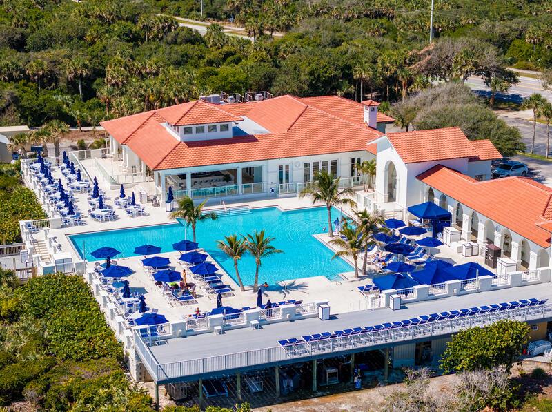 An aerial view shows a large clubhouse with a swimming pool and numerous patio umbrellas — VERO BEACH, FL