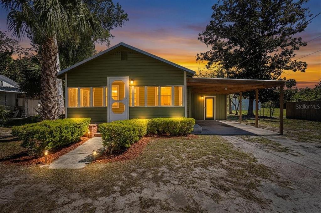 A green, single-story house with a front porch, carport, and landscaped yard at sunset — 102 NE 138TH STREET, CROSS CITY, FL