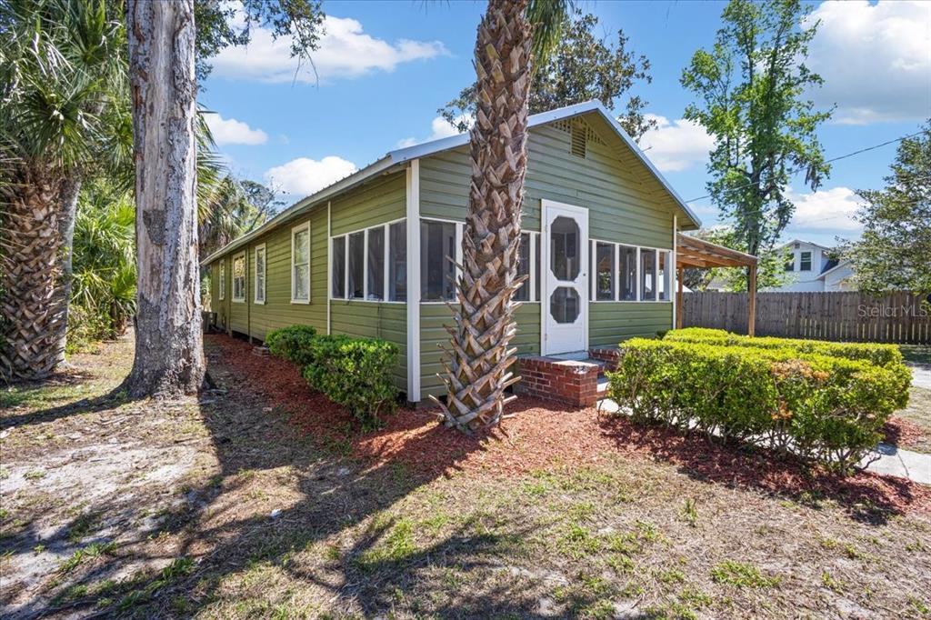 A green house with a screened-in porch, brick steps, and palm trees in the yard — 102 NE 138TH STREET, CROSS CITY, FL