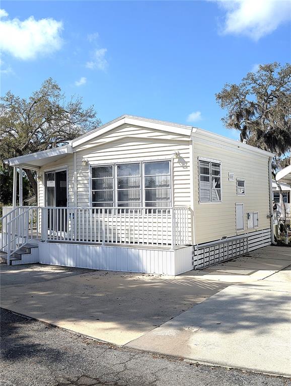 A light-colored manufactured home features a front porch with a white railing and stairs — 3300 26TH AVENUE E UNIT 228, BRADENTON, FL