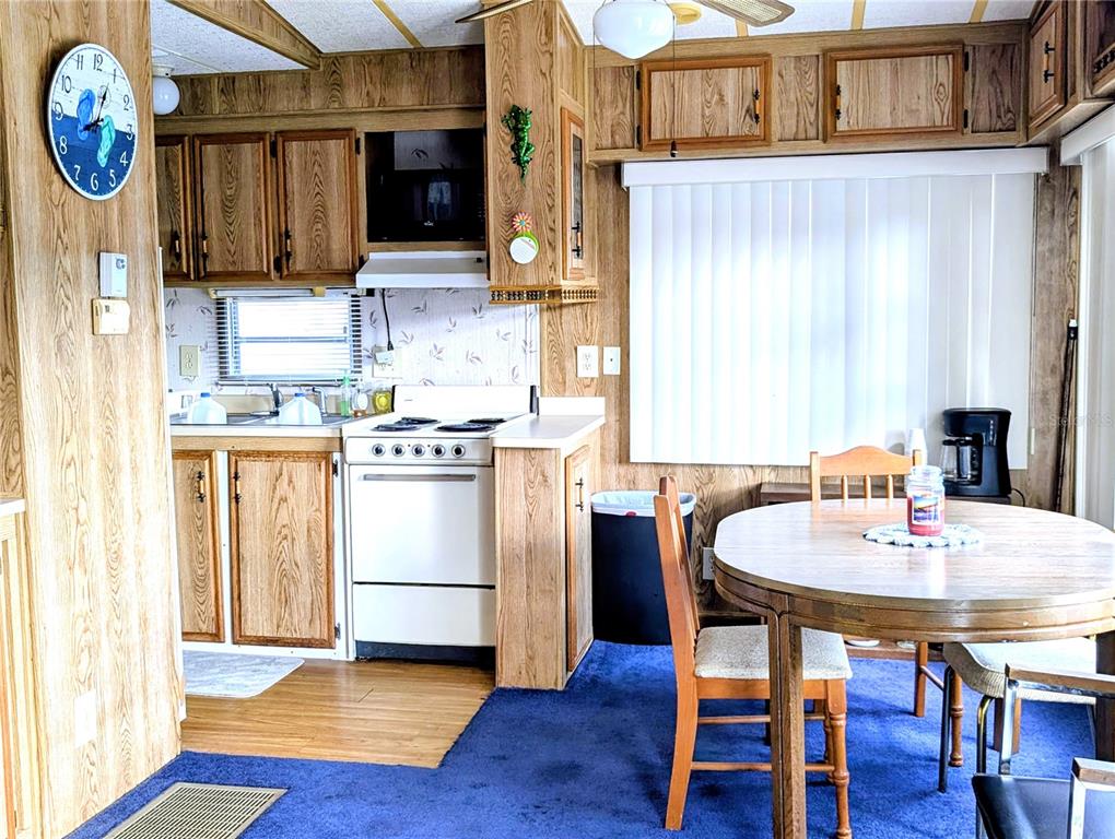 A kitchen and dining area feature wood cabinets, a white stove, and blue carpeting — 3300 26TH AVENUE E UNIT 228, BRADENTON, FL
