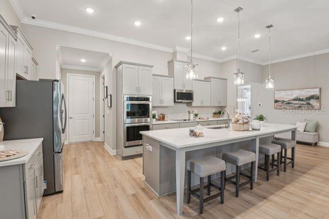 A modern kitchen features light gray cabinetry, a large white island with barstools, and stainless appliances — 3454 WINESAP WAY, LAKELAND, FL