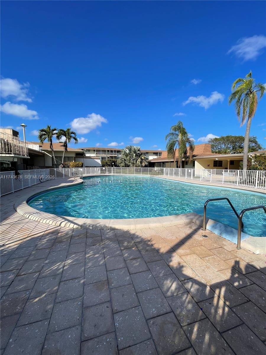 A swimming pool surrounded by a white fence and a paved patio with palm trees — 17090 NE 14th Ave # 314, Miami FL 33162, MIAMI, FL