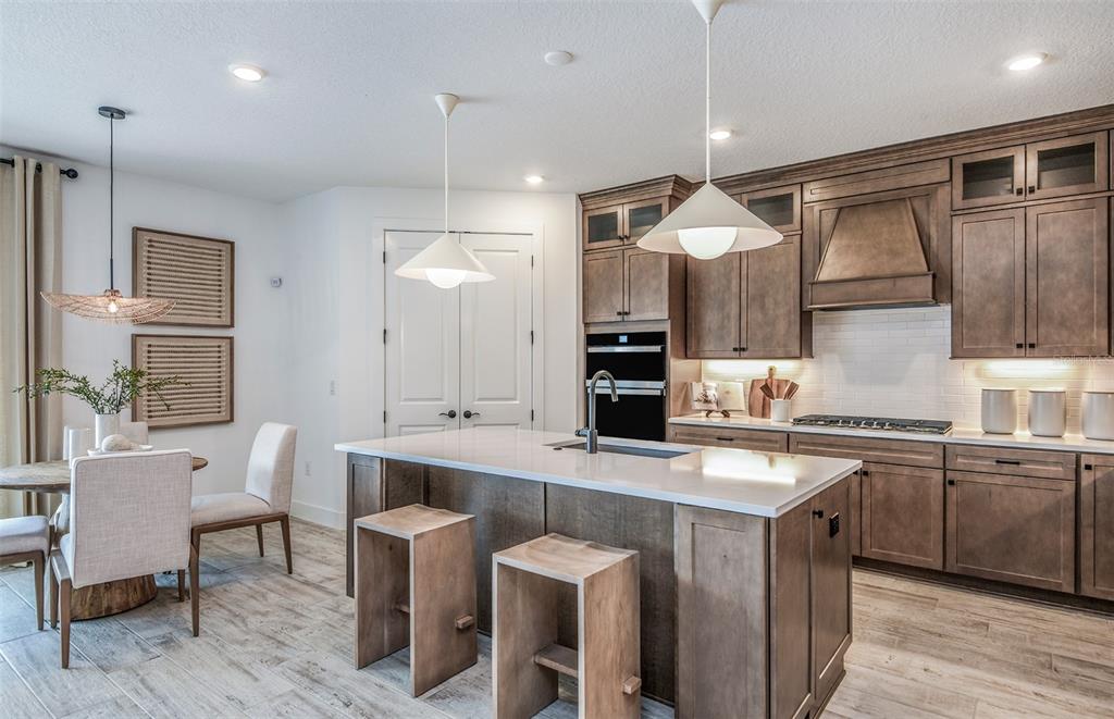 A kitchen features wood cabinets, a white quartz island with stools, and an adjacent dining area — 13710 BROOKSIDE HAVEN STREET, RIVERVIEW, FL