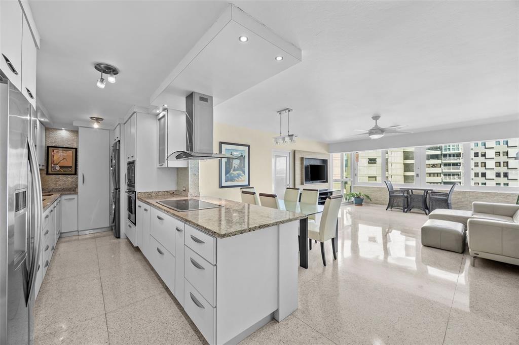 A modern open-concept kitchen and living area with white cabinetry, granite countertops, and tile flooring — 4429 AVE. ISLA VERDE UNIT 1103, CAROLINA, PR
