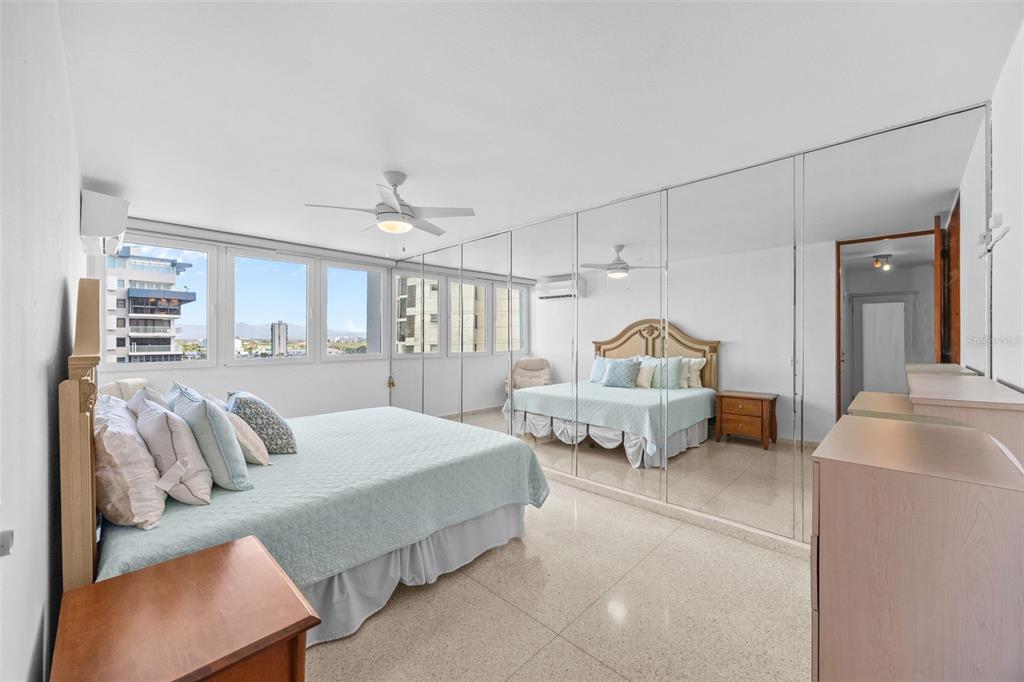 A bedroom features a bed, tiled floors, mirrored closet doors, and large windows with city views — 4429 AVE. ISLA VERDE UNIT 1103, CAROLINA, PR