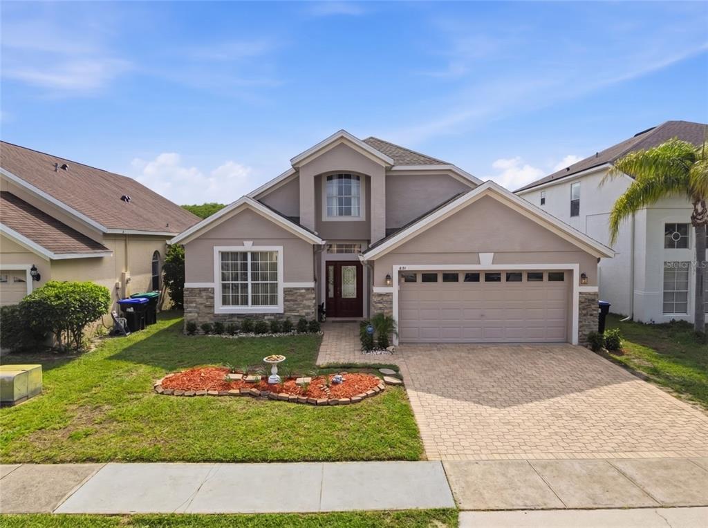 A two-story suburban house features a beige stucco exterior, stone accents, and a paved driveway — 831 WHISPERING CYPRESS LANE, ORLANDO, FL