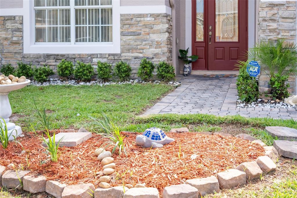 A stone-veneer house exterior features a red front door, a paved walkway, and landscaping — 831 WHISPERING CYPRESS LANE, ORLANDO, FL