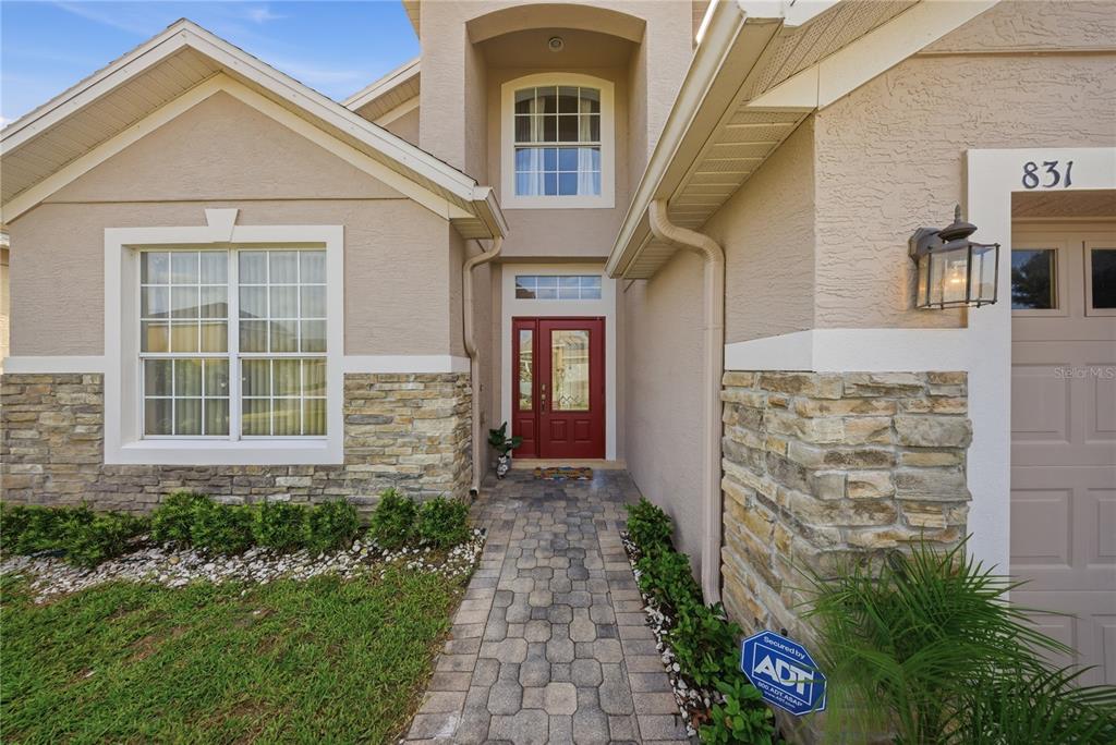 A beige house exterior features a red front door, stone veneer, and a paver walkway — 831 WHISPERING CYPRESS LANE, ORLANDO, FL