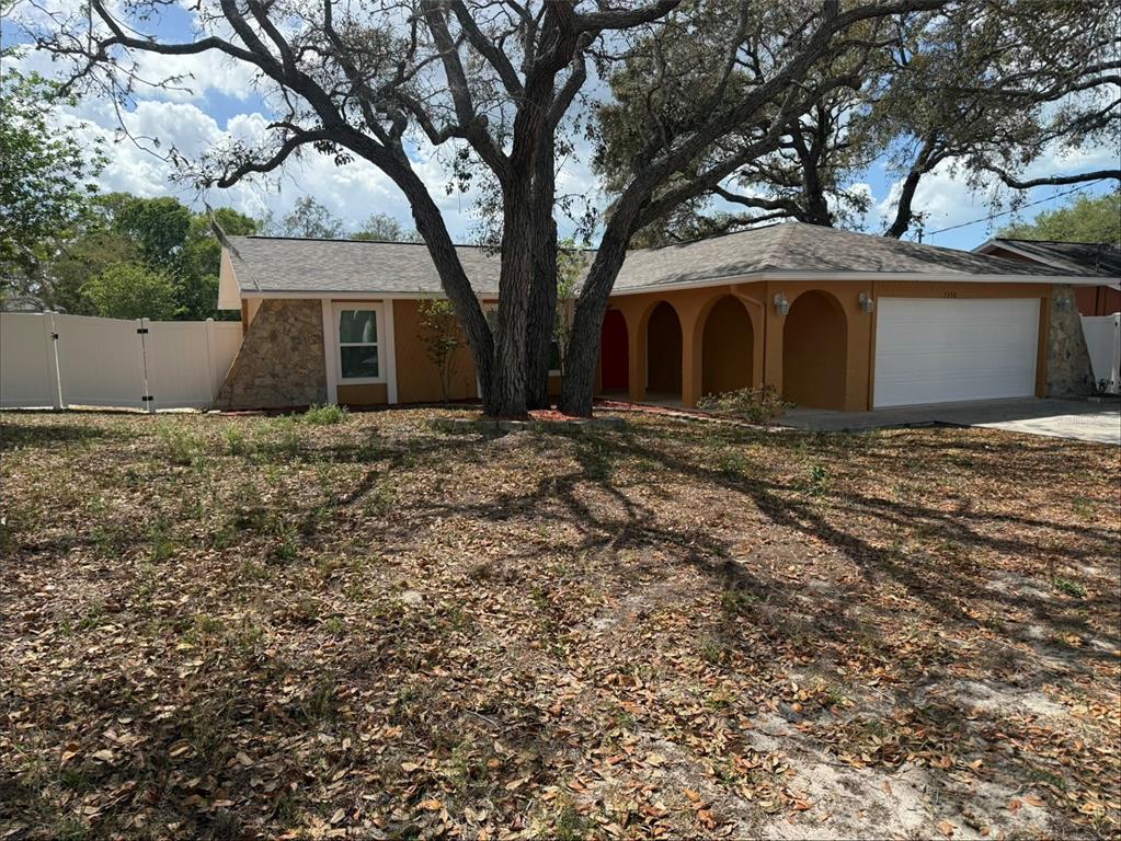 A single-story house with an orange stucco exterior, stone accents, and a large tree — 7350 LANDMARK DRIVE, SPRING HILL, FL