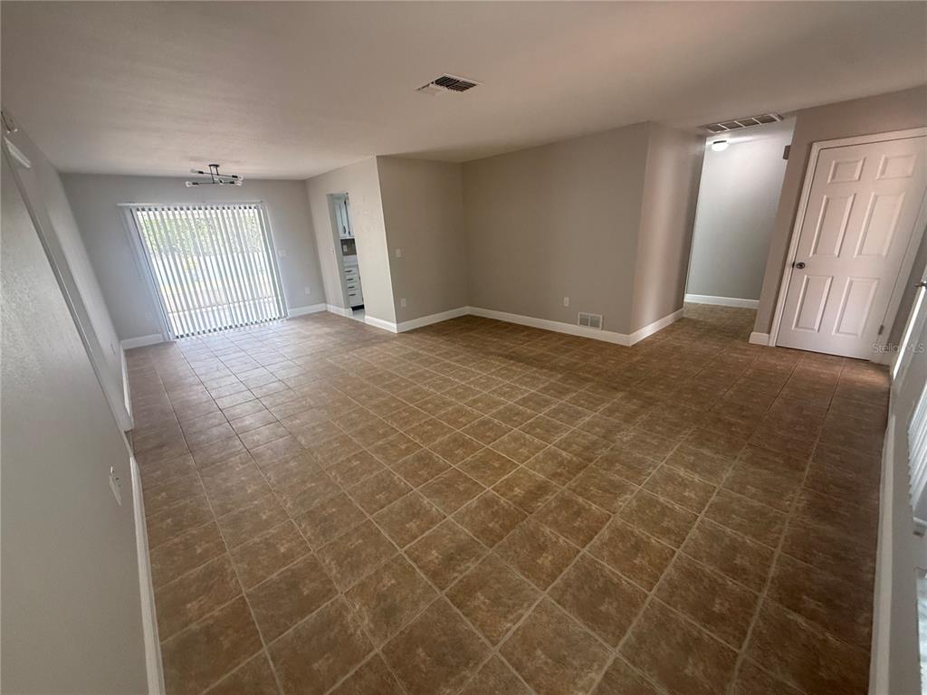 An empty room with light gray walls, brown tile flooring, and a sliding glass door — 7350 LANDMARK DRIVE, SPRING HILL, FL