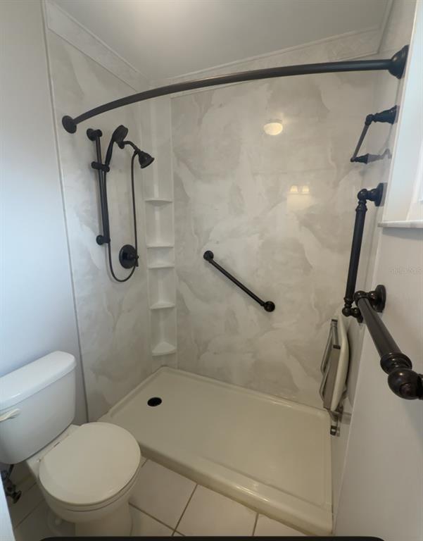 A bathroom features a walk-in shower with a grab bar, folding seat, and dark fixtures — 7350 LANDMARK DRIVE, SPRING HILL, FL