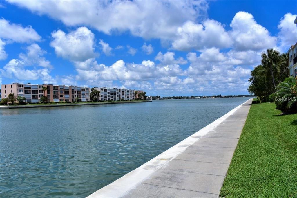 A concrete walkway runs along a grassy bank beside a wide canal with apartment buildings — 7420 BAY ISLAND DRIVE S UNIT 176, SOUTH PASADENA, FL