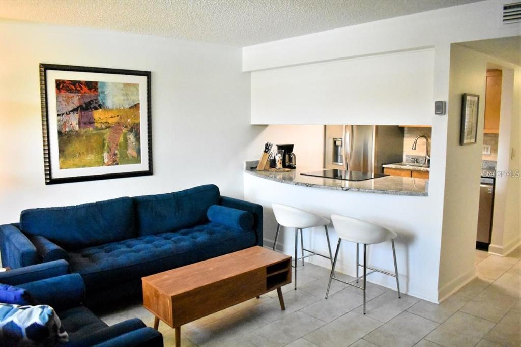 A living room with a blue sofa, wooden coffee table, and a kitchen breakfast bar — 7420 BAY ISLAND DRIVE S UNIT 176, SOUTH PASADENA, FL