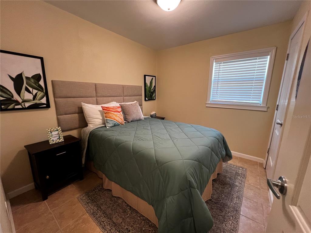 A bedroom features a queen bed with a tufted headboard, tile flooring, and a window — 138 WOODS ROAD, SAN MATEO, FL