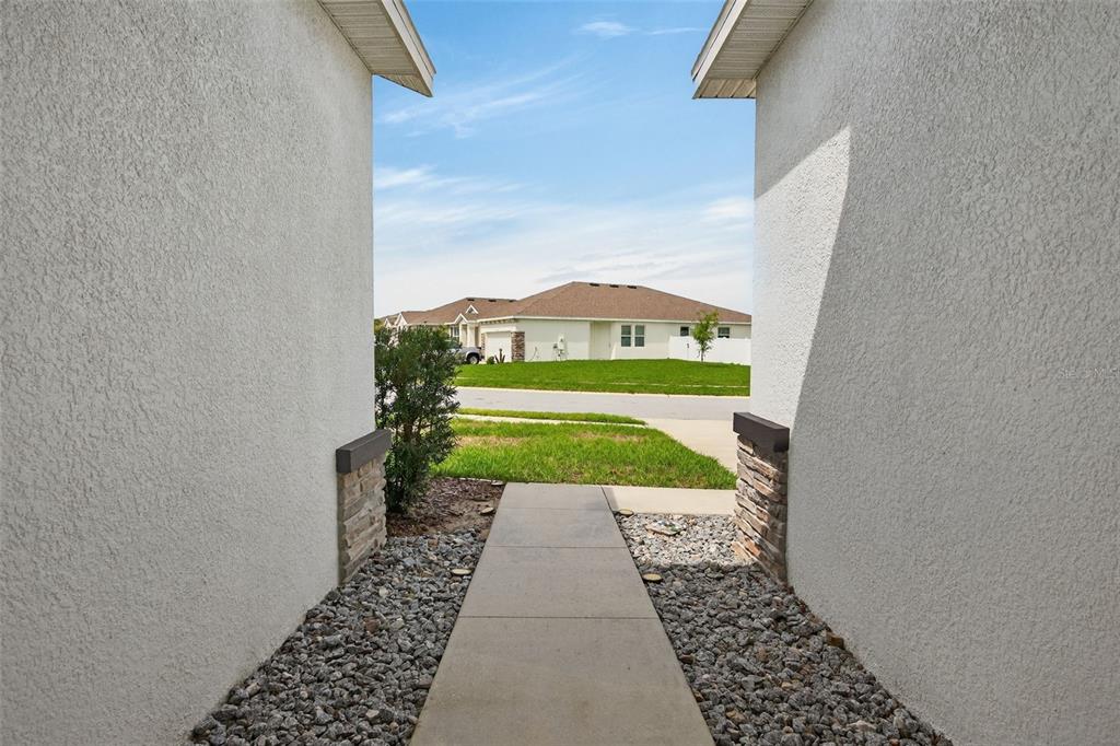 A concrete walkway leads from a covered entryway toward a suburban street and neighboring houses — 13454 GOLDEN LIME AVENUE, SPRING HILL, FL