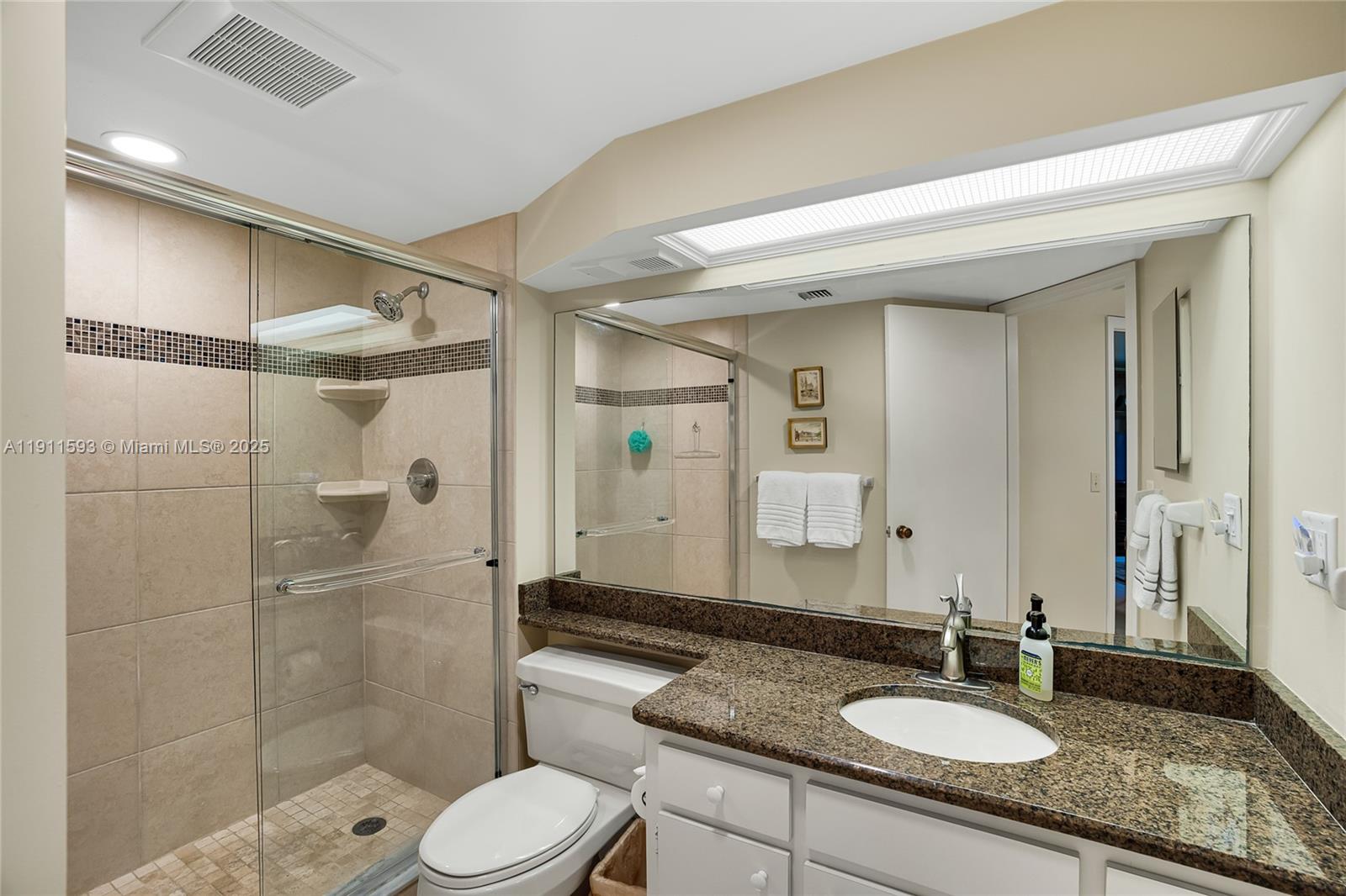 A bathroom features a glass-enclosed shower, a granite vanity countertop, and a large wall mirror — 1815 Mooringline Dr # 1, Vero Beach FL 32963, VERO BEACH, FL