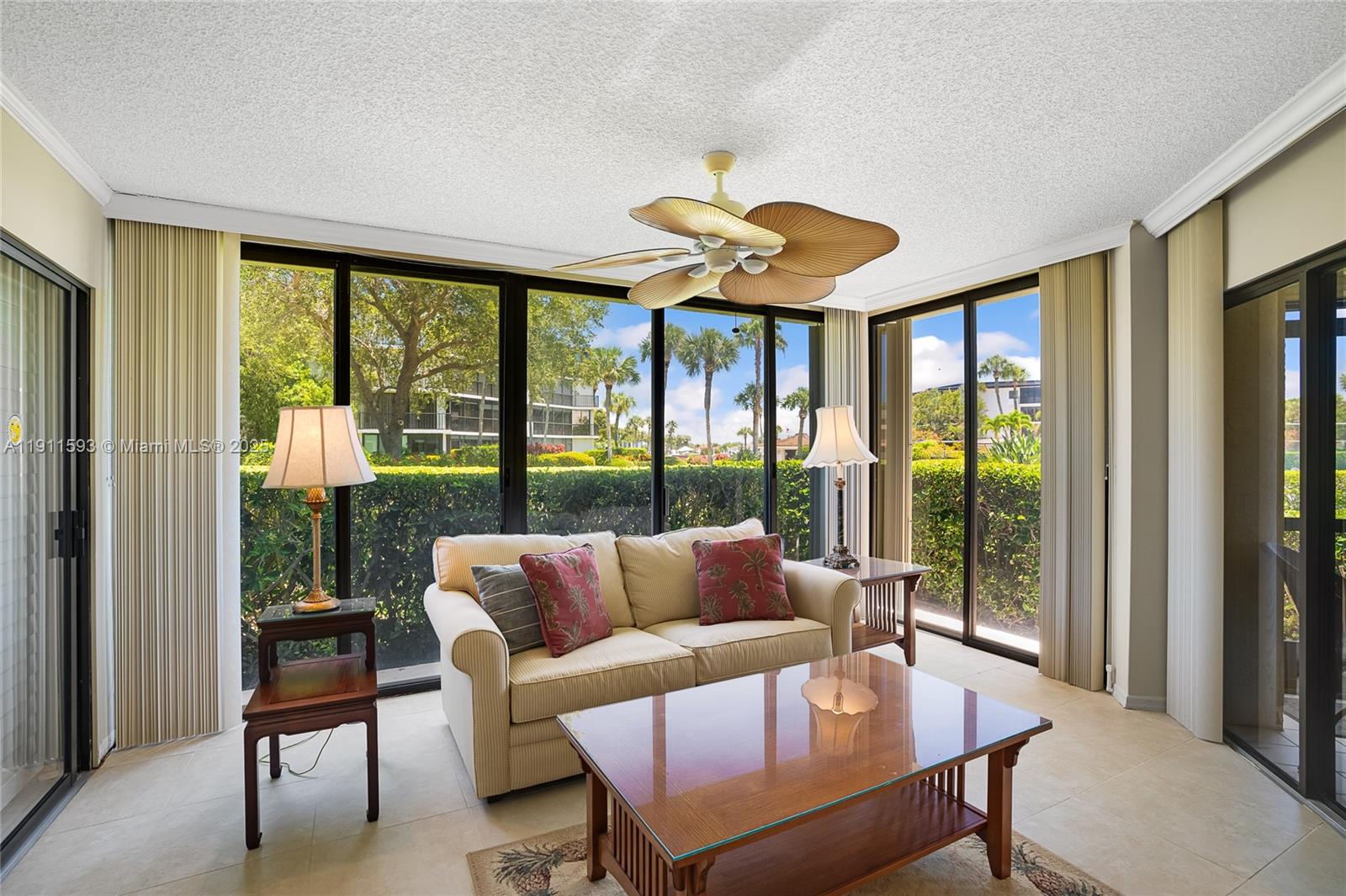 A sunroom features a beige sofa, glass coffee table, and large windows overlooking palm trees — 1815 Mooringline Dr # 1, Vero Beach FL 32963, VERO BEACH, FL
