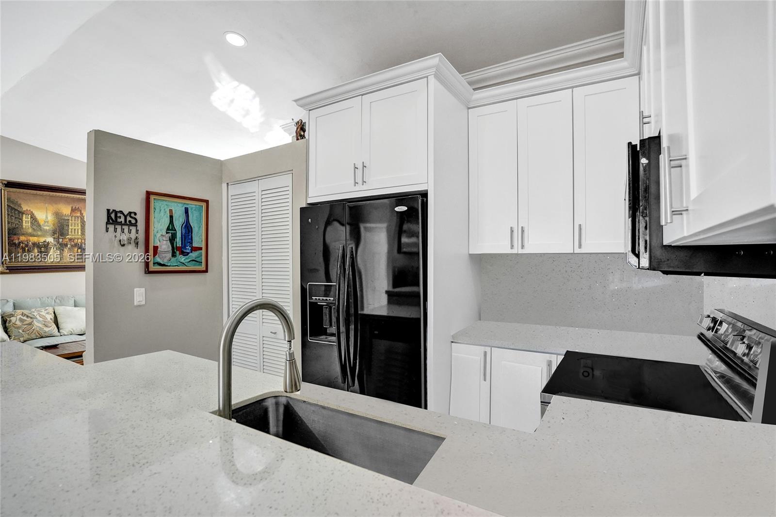 A modern kitchen features white cabinetry, a black refrigerator, and light gray quartz countertops — 6405 SW 152nd Cir Pl # 05, Miami FL 33193, MIAMI, FL
