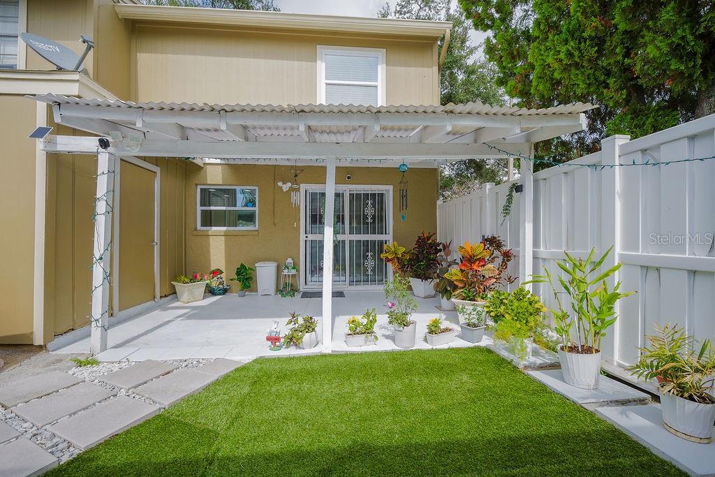 A patio features a white pergola, artificial turf, potted plants, and a sliding glass door — 6902 SOLEDAD COURT, TAMPA, FL