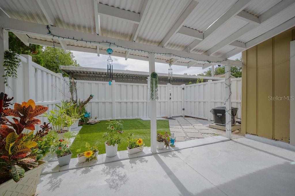 A covered patio overlooks a small backyard with artificial turf and a white privacy fence — 6902 SOLEDAD COURT, TAMPA, FL