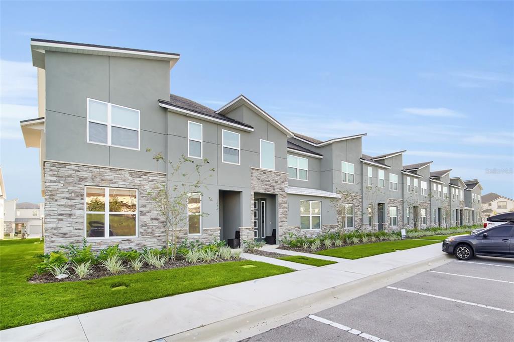 A multi-unit townhouse building features gray stucco walls, stone veneer accents, and a paved parking lot — 1672 TROPICAL PALMS CIRCLE, KISSIMMEE, FL