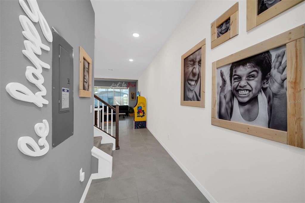 A hallway with gray tile flooring, framed black-and-white photos, and a wall-mounted electrical panel — 1672 TROPICAL PALMS CIRCLE, KISSIMMEE, FL