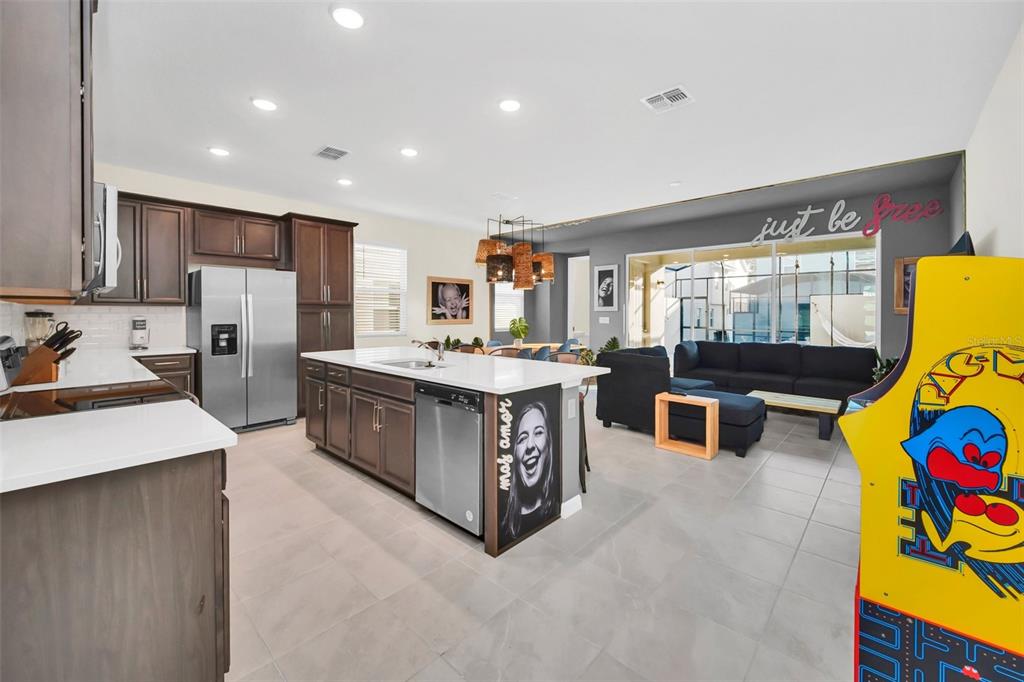 A modern open-concept kitchen with dark cabinets, a white island, and a living area beyond — 1672 TROPICAL PALMS CIRCLE, KISSIMMEE, FL