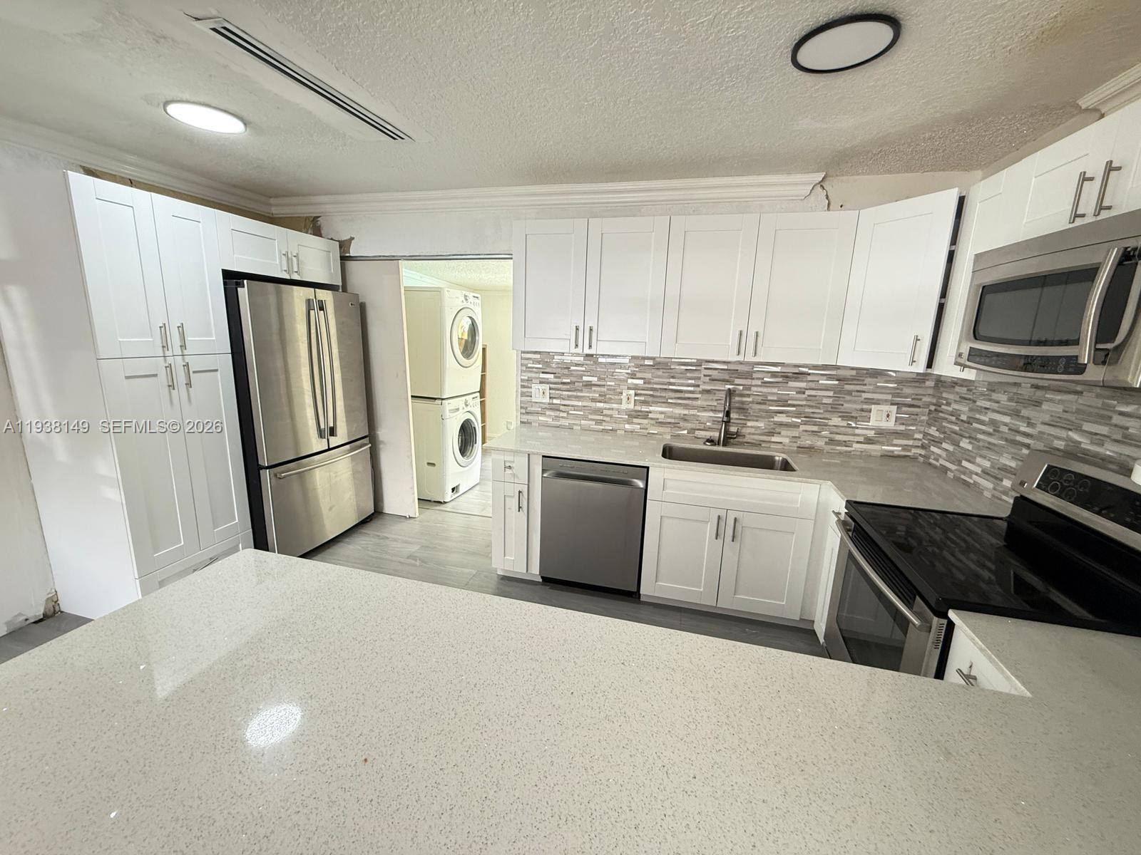 A modern kitchen features white cabinetry, stainless steel appliances, and a quartz countertop island — 4361 SW 49th Ct, Dania Beach FL 33314, DANIA BEACH, FL