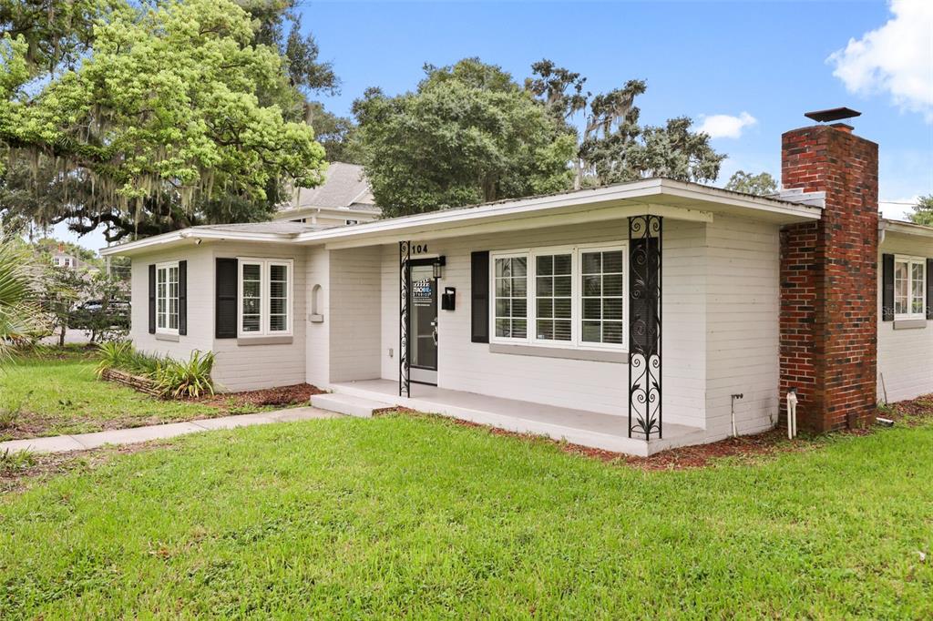 A single-story house with a brick chimney, white painted brick exterior, and a front porch — 104 S CLYDE AVENUE, KISSIMMEE, FL