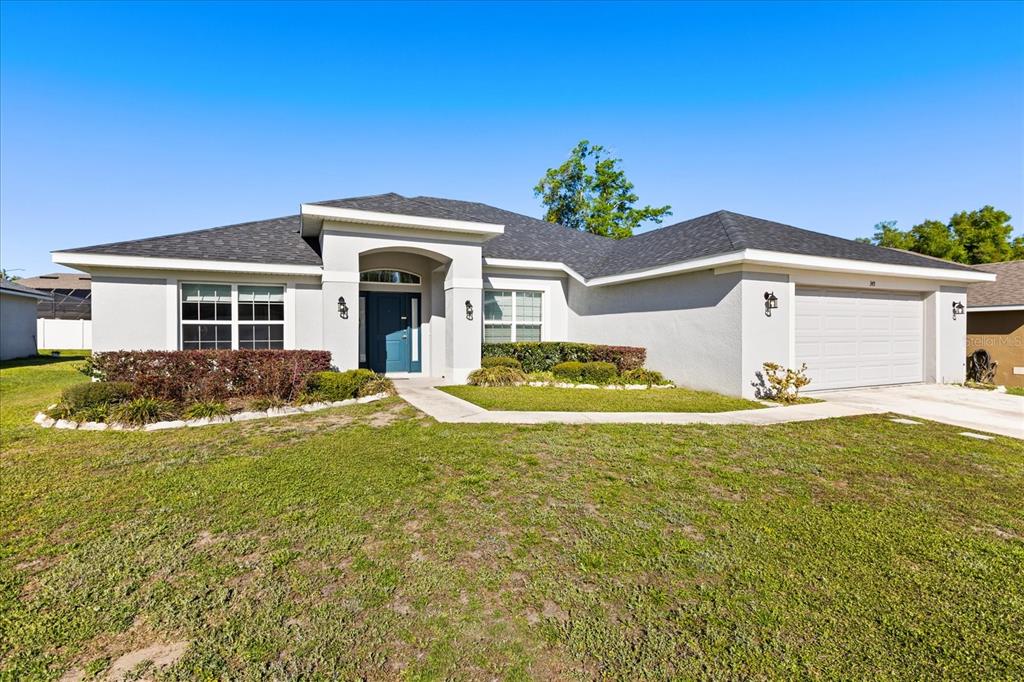A single-story suburban house with a gray stucco exterior, dark roof, and two-car garage — 345 ASHTON WOODS LANE, LEESBURG, FL
