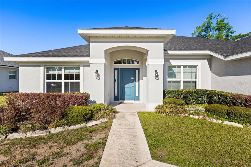 The exterior of a single-story house features a blue front door and a concrete walkway — 345 ASHTON WOODS LANE, LEESBURG, FL