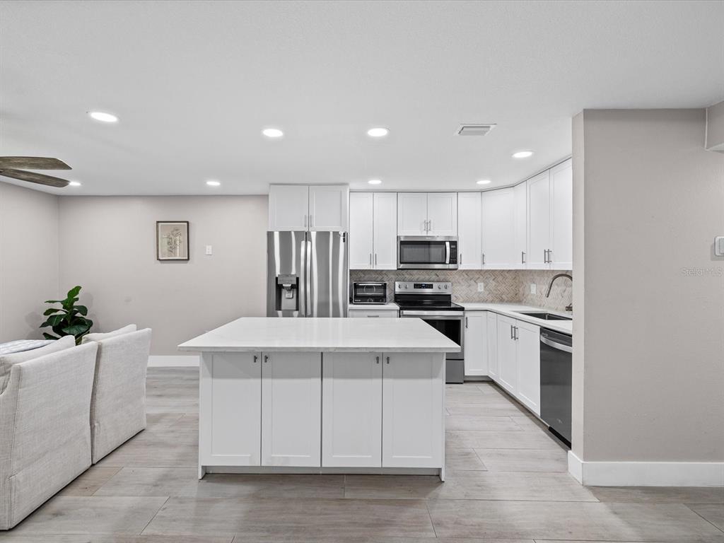 A modern kitchen features white cabinets, a central island, and light wood-look flooring — 4335 AEGEAN DRIVE UNIT 128A, TAMPA, FL