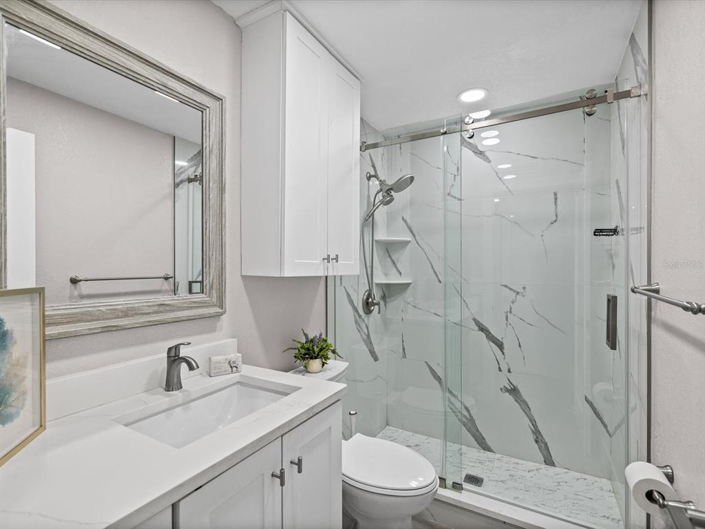 A bathroom features a white vanity, a toilet, and a glass-enclosed shower with marble-look tile — 4335 AEGEAN DRIVE UNIT 128A, TAMPA, FL