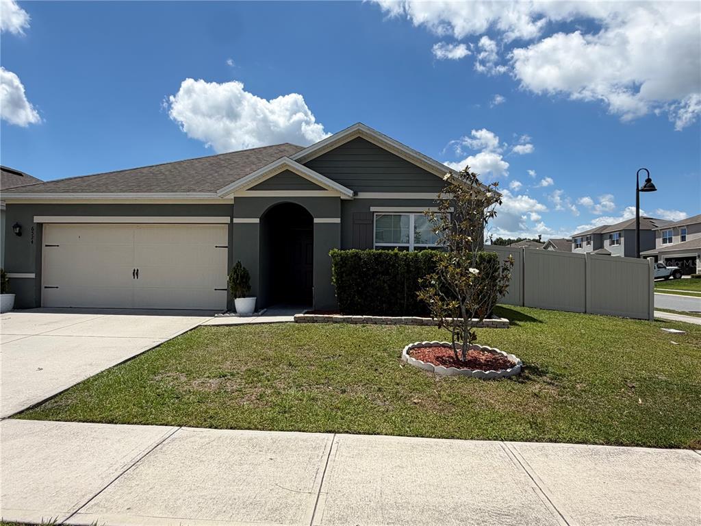 A single-story house with a gray exterior, a two-car garage, and a small front yard — 6524 CORAL BERRY DRIVE, MOUNT DORA, FL
