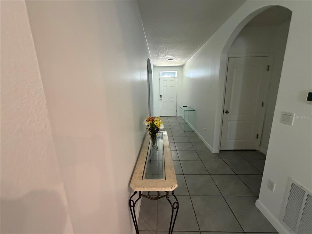 A tiled hallway leads to a front door with a glass-topped console table in the foreground — 6524 CORAL BERRY DRIVE, MOUNT DORA, FL