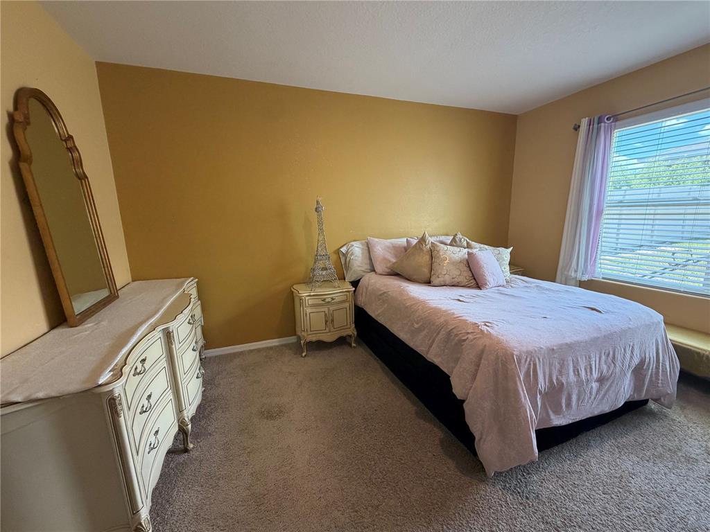 A bedroom features a bed, a dresser with a mirror, and gold-toned walls — 6524 CORAL BERRY DRIVE, MOUNT DORA, FL