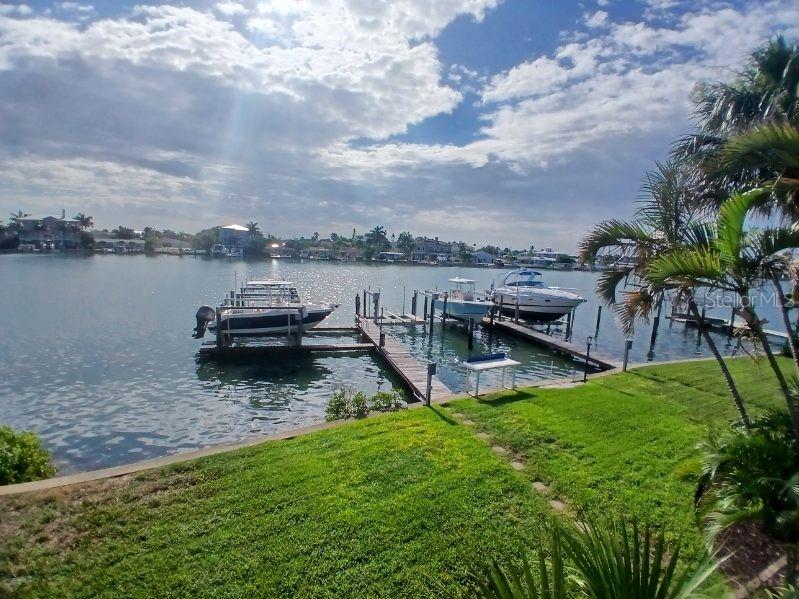 A view of a grassy backyard leading to a private boat dock with three boats — 2505 BAY BOULEVARD UNIT 1, INDIAN ROCKS BEACH, FL