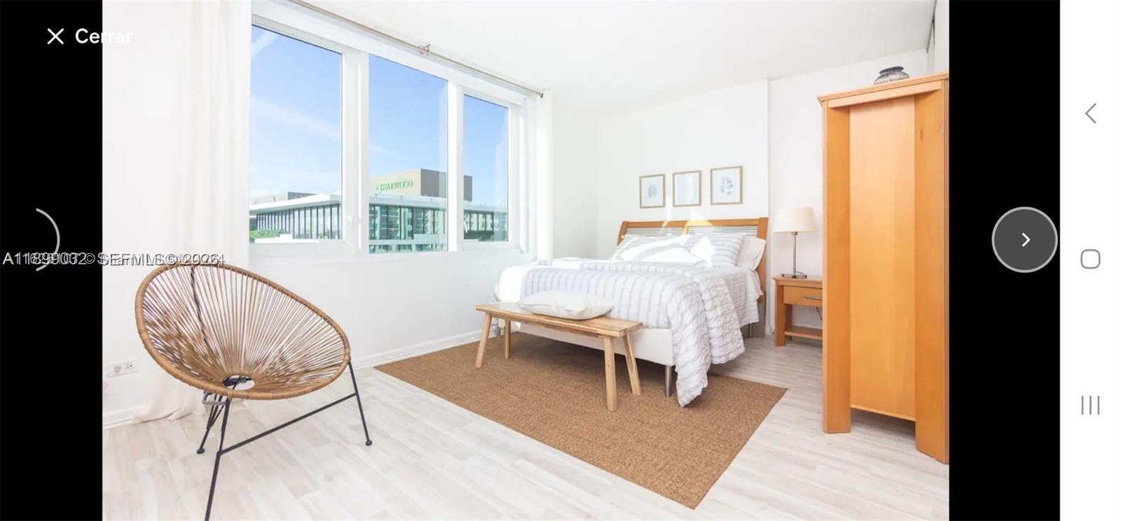A bedroom features a bed, a wooden bench, a rattan chair, and large windows — 2301 Collins Ave # 736, Miami Beach FL 33139, MIAMI BEACH, FL